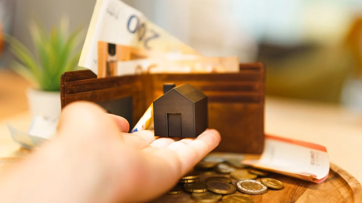 Mano con una casa en miniatura delante de una cartera con billetes de euro, deducción por alquiler de vivienda habitual