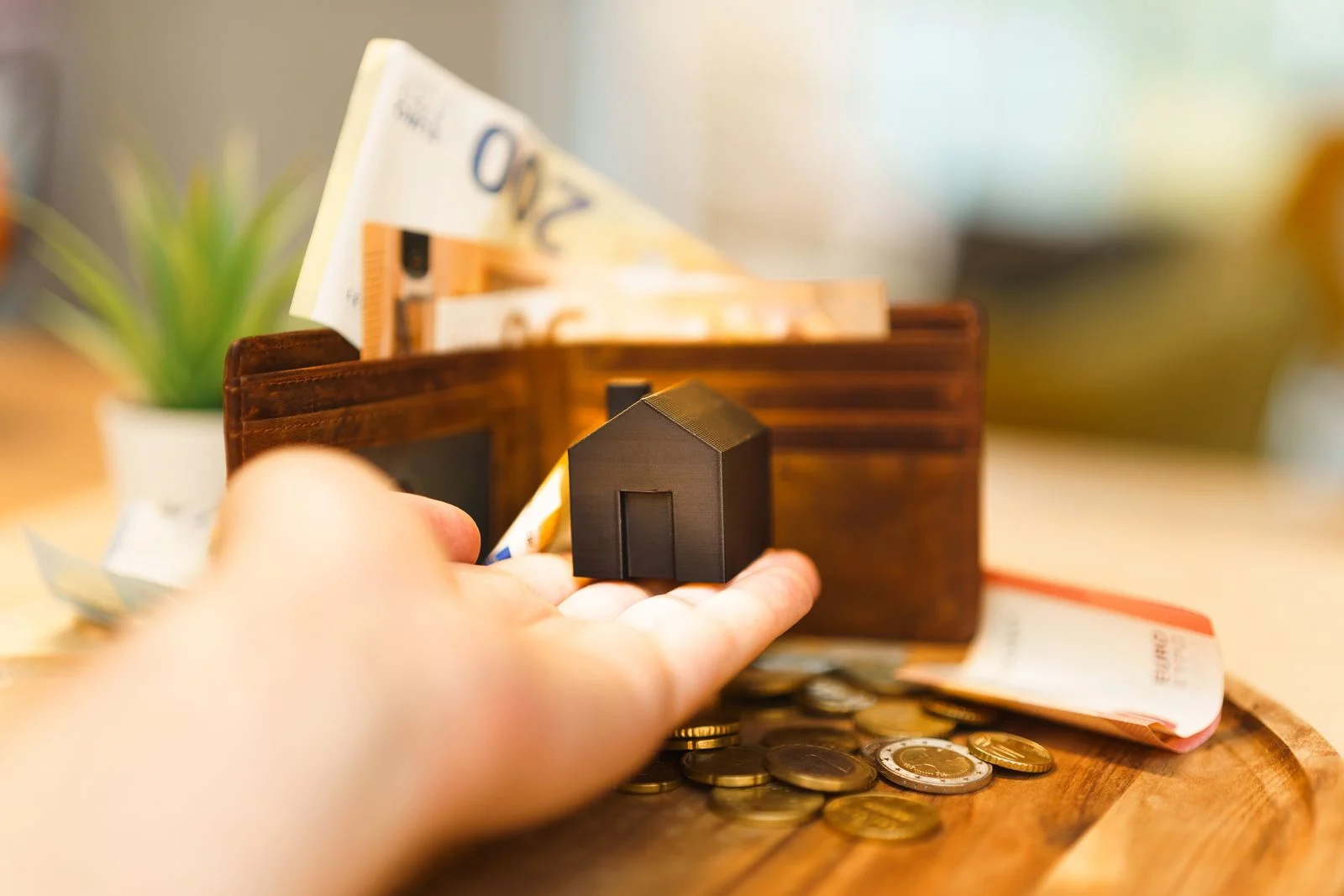 Mano con una casa en miniatura delante de una cartera con billetes de euro, deducción por alquiler de vivienda habitual