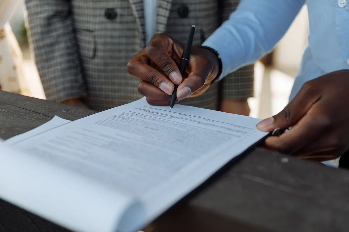 Dos personas firman la escritura de compraventa de una vivienda sobre una mesa de madera